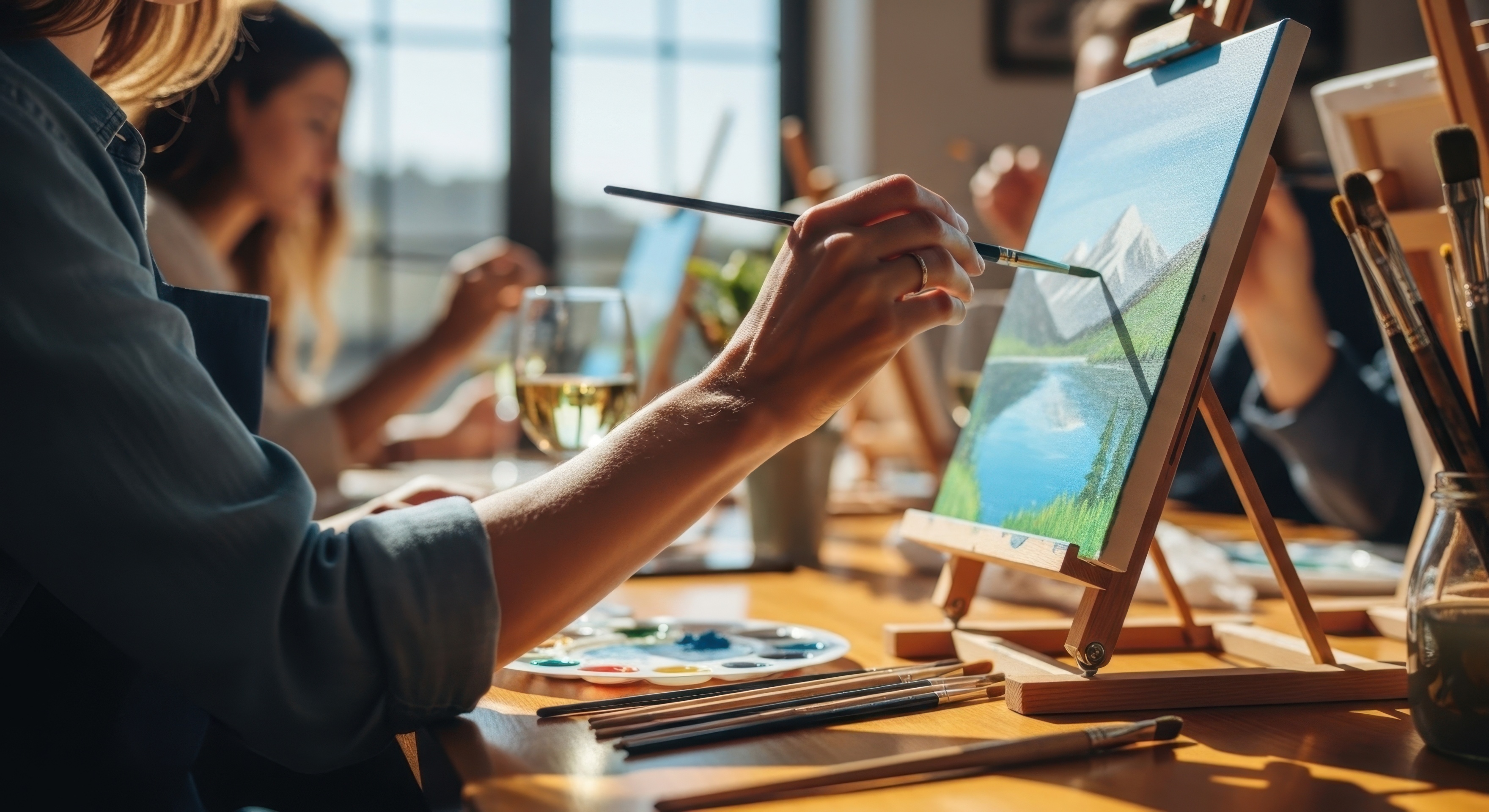 Students at easels in a sunlit painting class, brushes in hand.