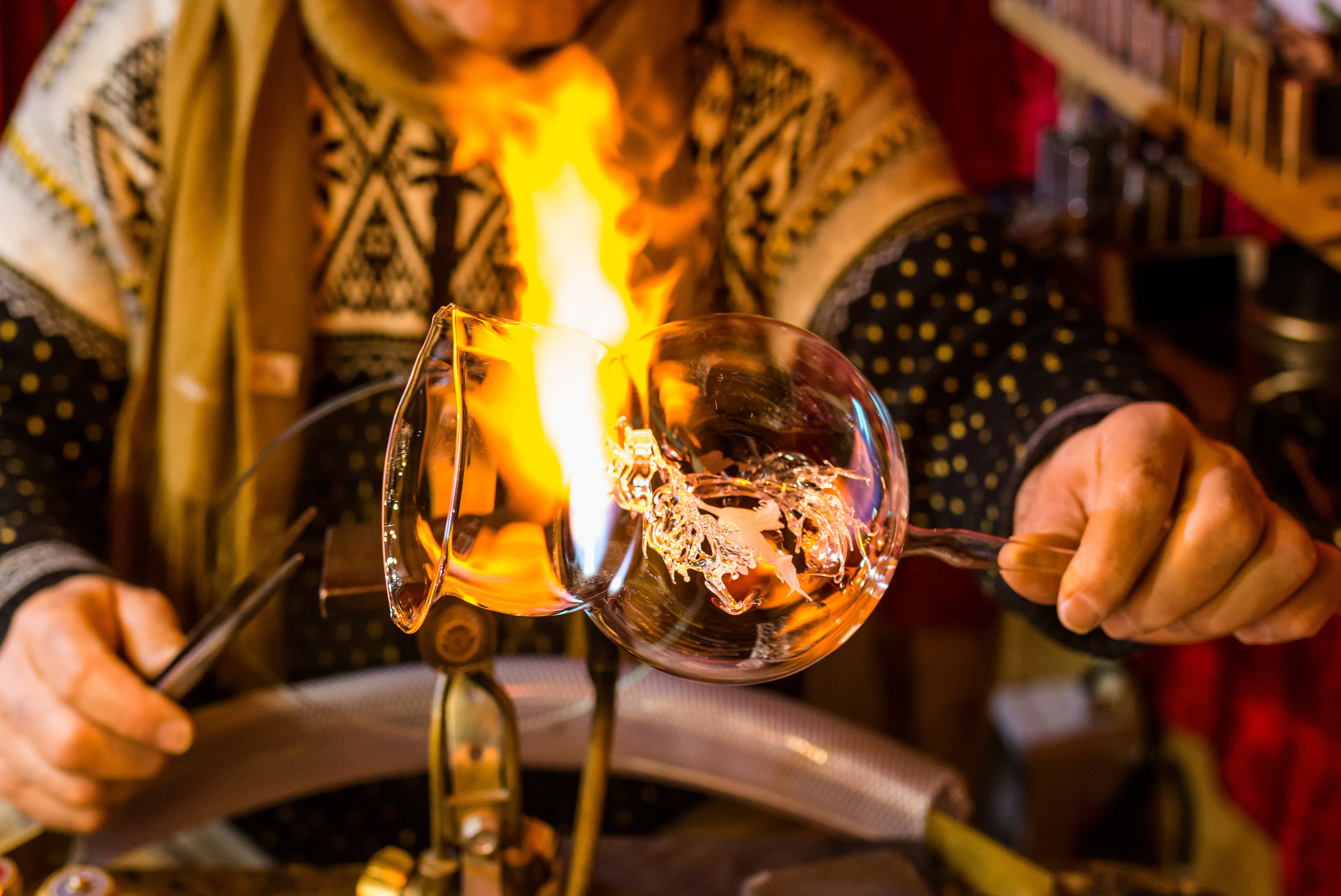 Molten glass glowing on a punty rod with flame nearby in a hot shop.