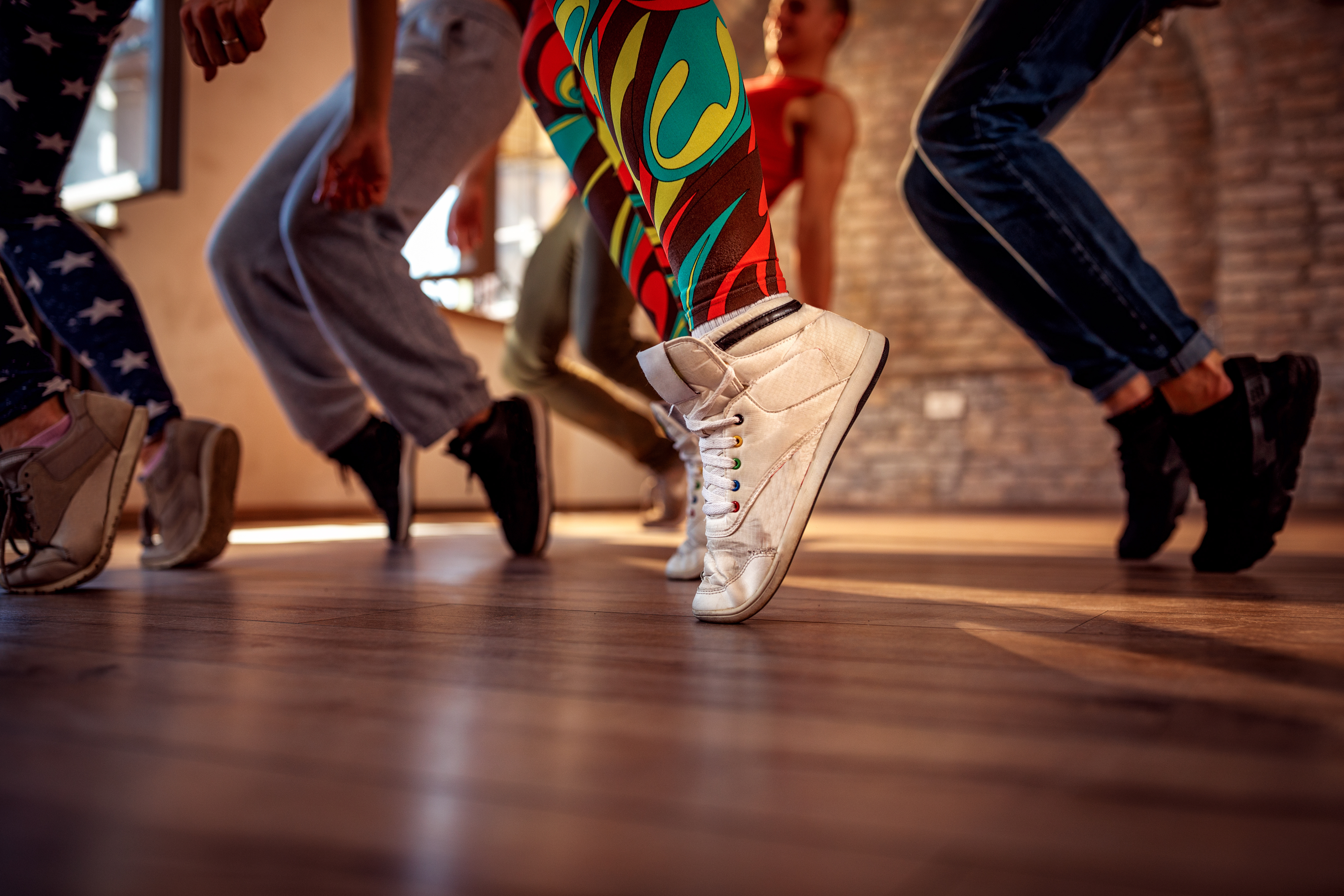 Close-up of dancers' sneakers mid-step on a warm hardwood studio floor.
