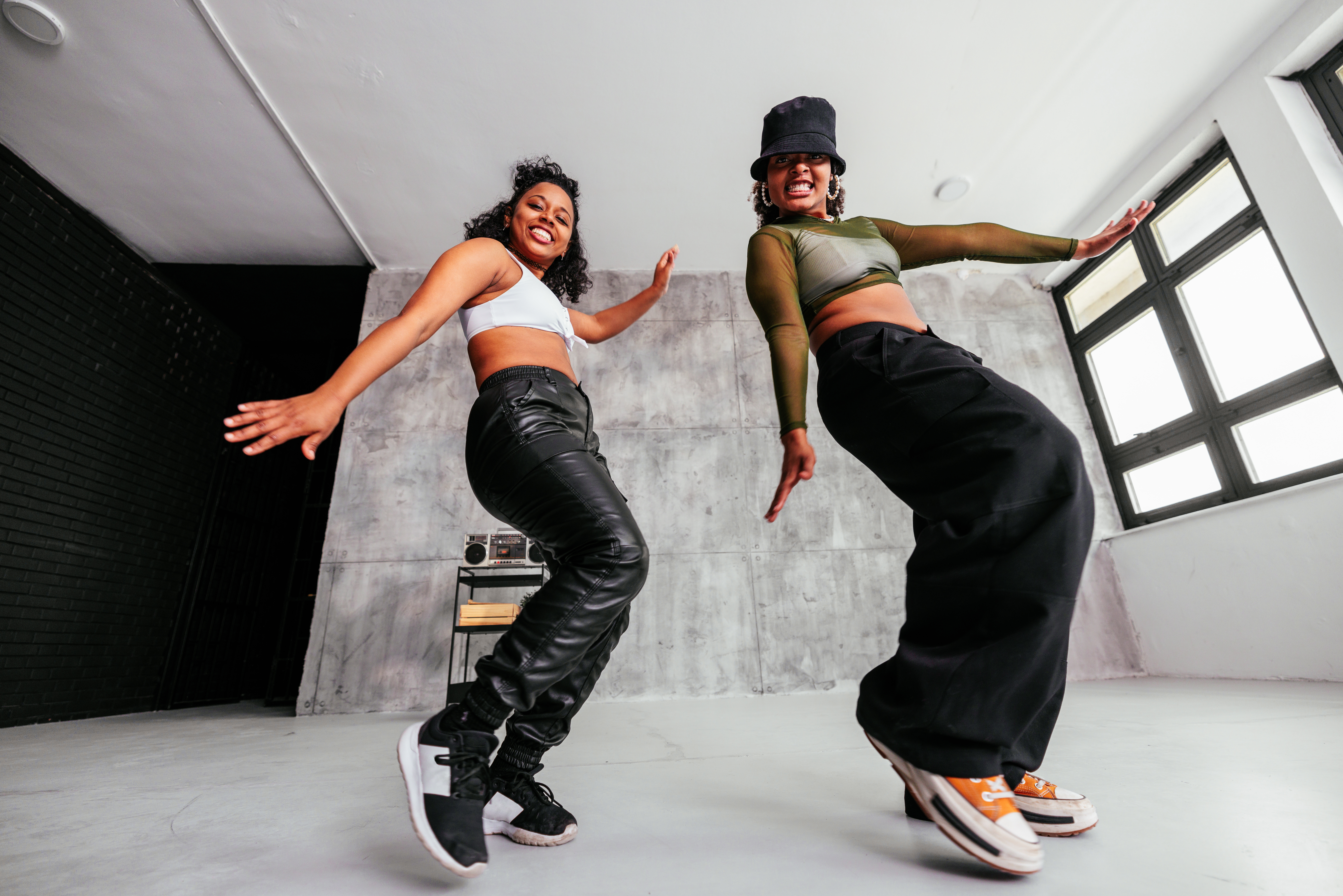 Two hip-hop dancers mid-pose in a concrete-walled urban dance studio.